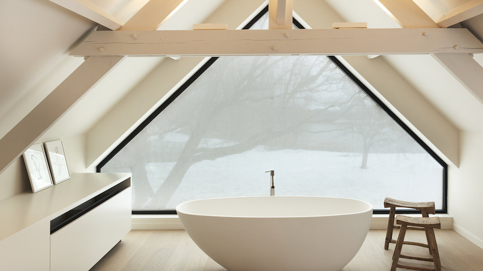 Badezimmer mit freistehender Badewanne vor einem grossen Dreiecksfenster mit Sichtschutztextil.