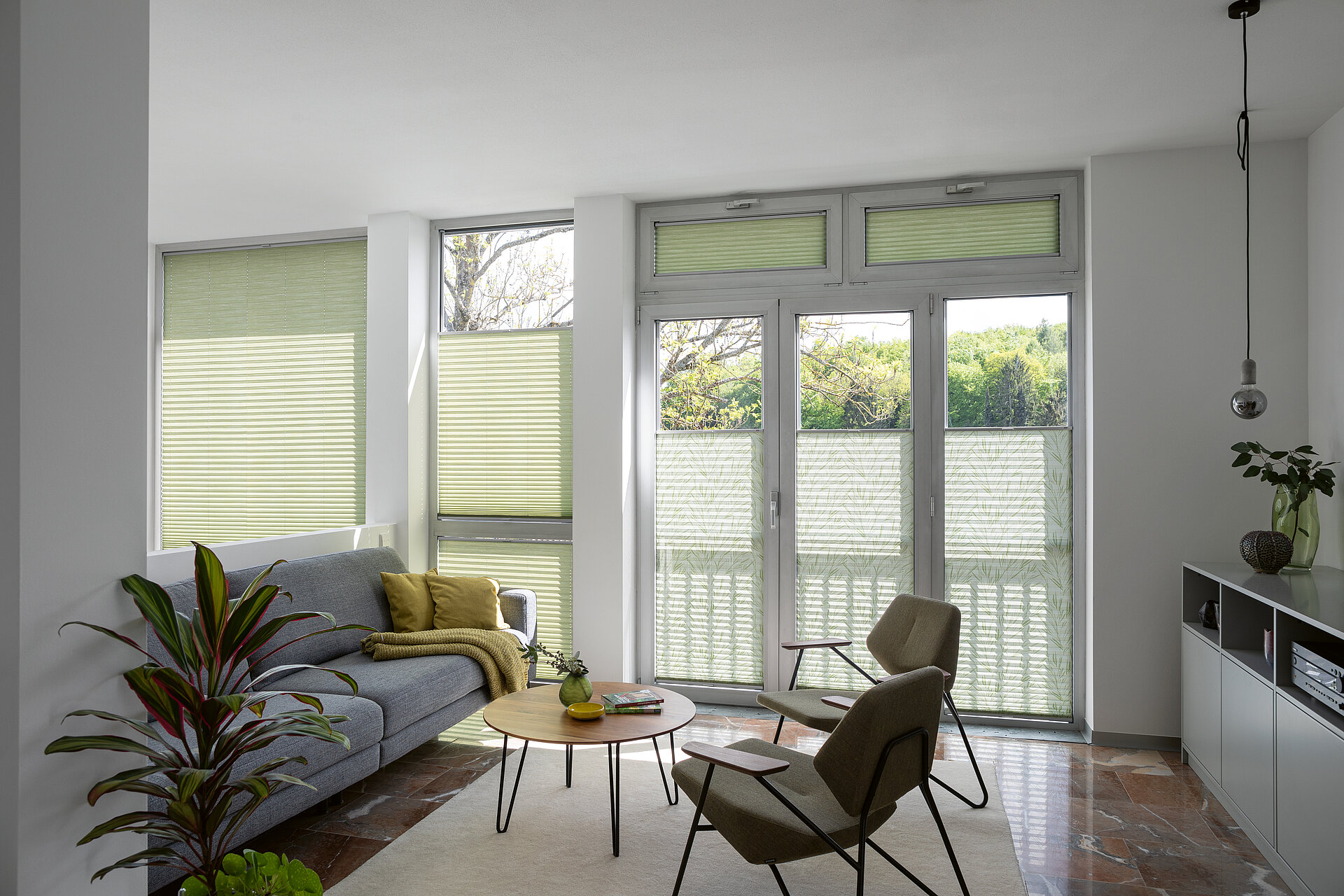 Grüne Plissees mit einfarbigen und floralen Bereichen in hellem Wohnzimmer mit bodentiefen Fenstern.